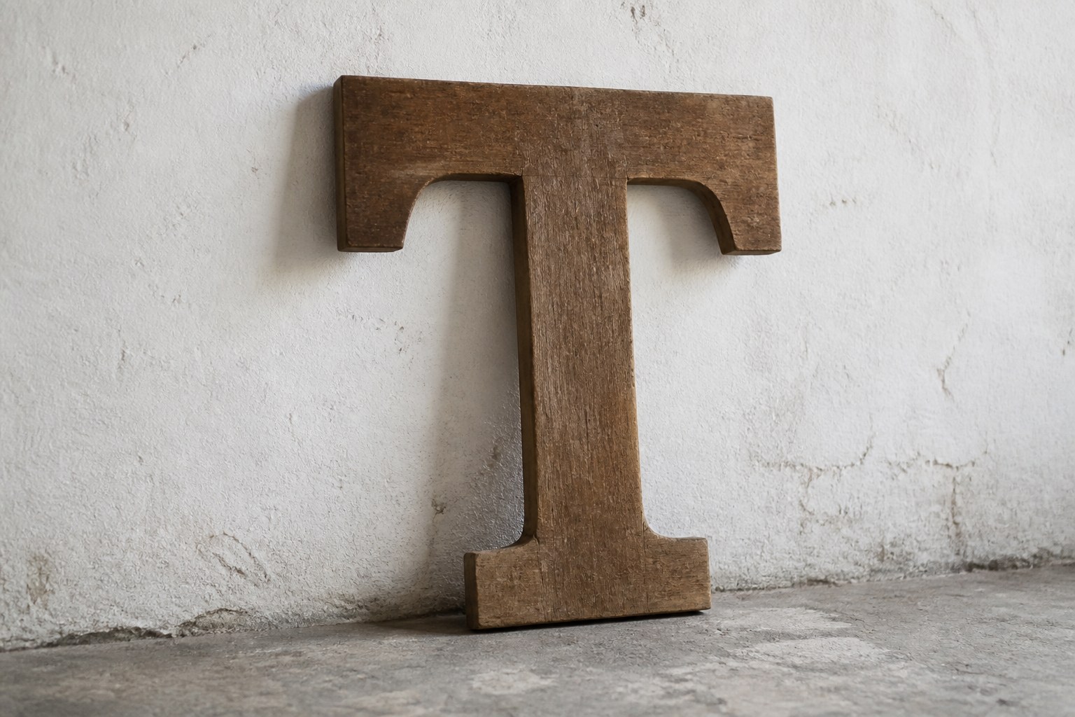 A large wooden poster type capital letter T leaning against a whitewashed wall