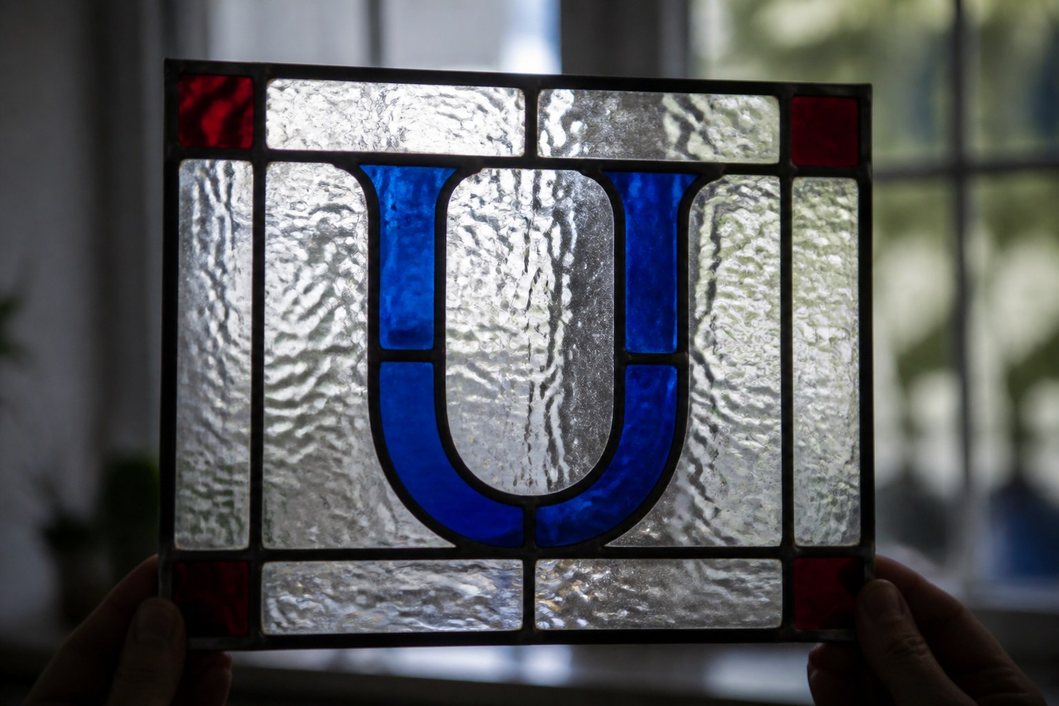 The capital letter U formed from leaded came in a small stained glass panel held up to the light