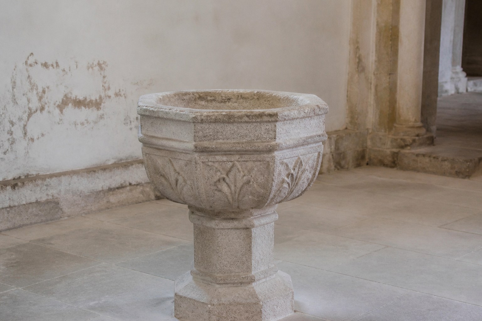 A plain carved stone baptismal font standing empty in a bare church