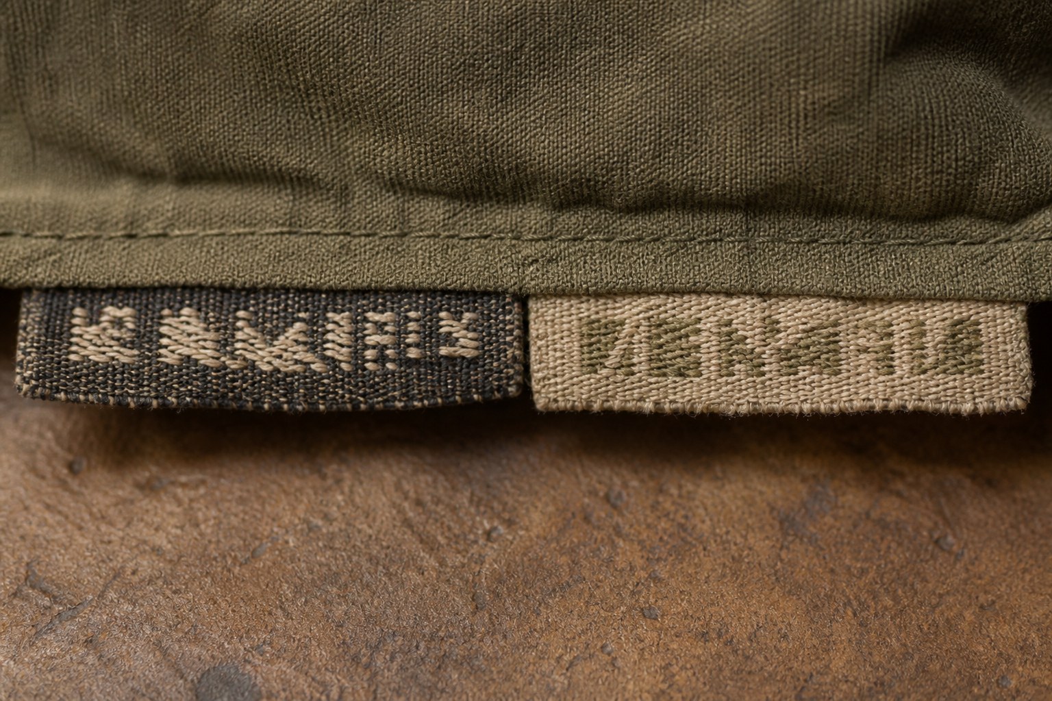 Two woven name tapes sewn into a garment hem with slightly different lettering