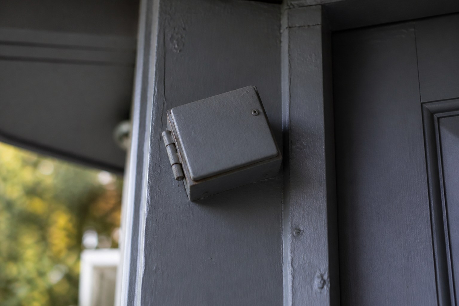 A small metal case fixed at an angle to the upper part of a painted doorpost
