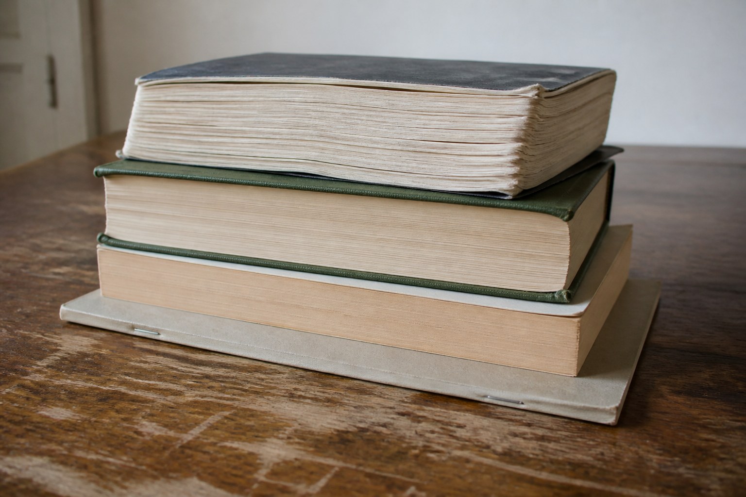 Books of visibly different kinds stacked on a table, from a thick thin-paper volume down to a slim one