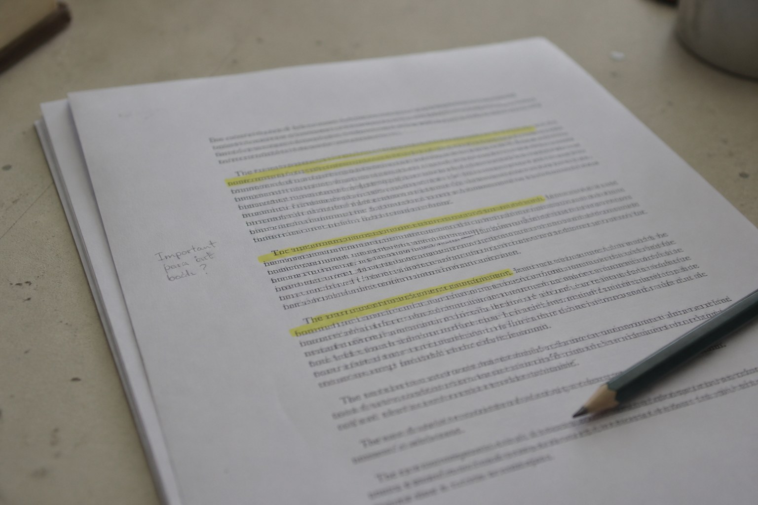 A printed page on a desk with three short passages marked in pale yellow highlighter and a pencil note in the margin, the text too small to read, a pencil lying across one corner