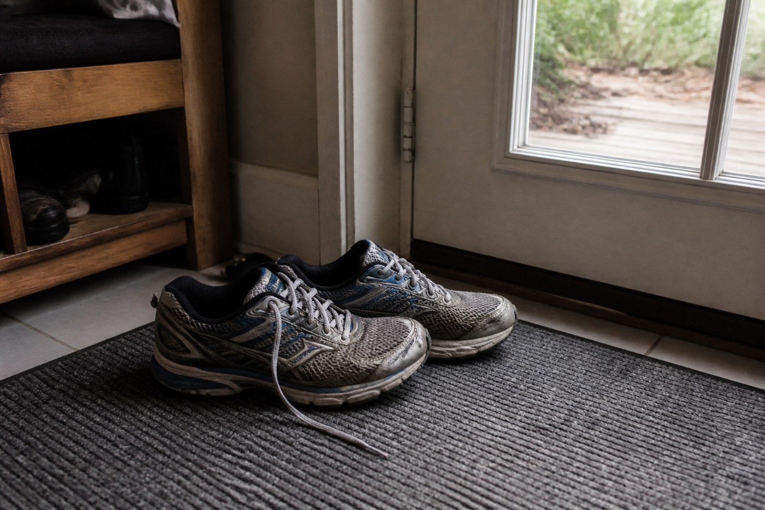 A pair of running shoes by a door with one lace still untied