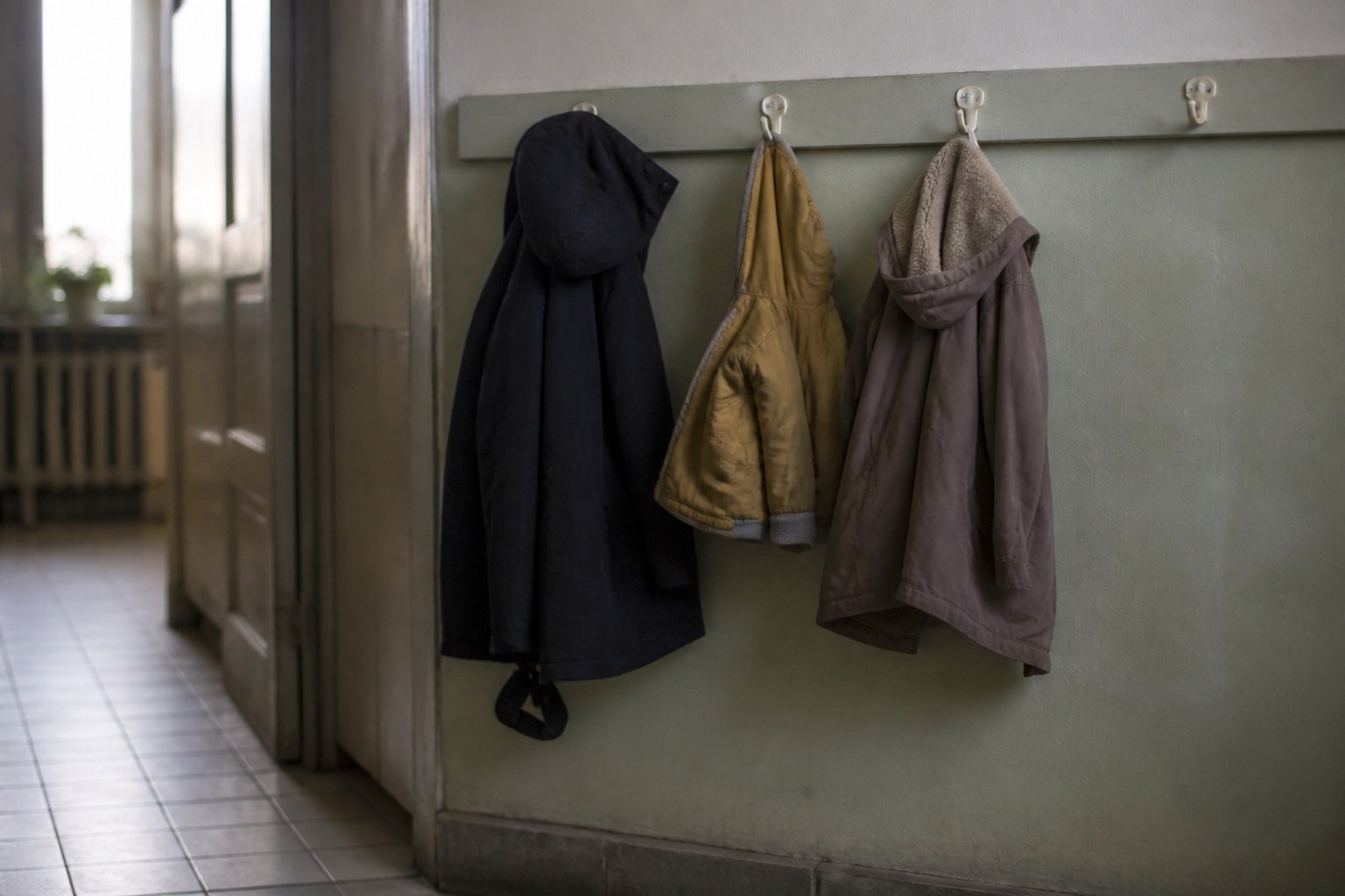 Three coats of different sizes on a row of hooks in a cold hallway