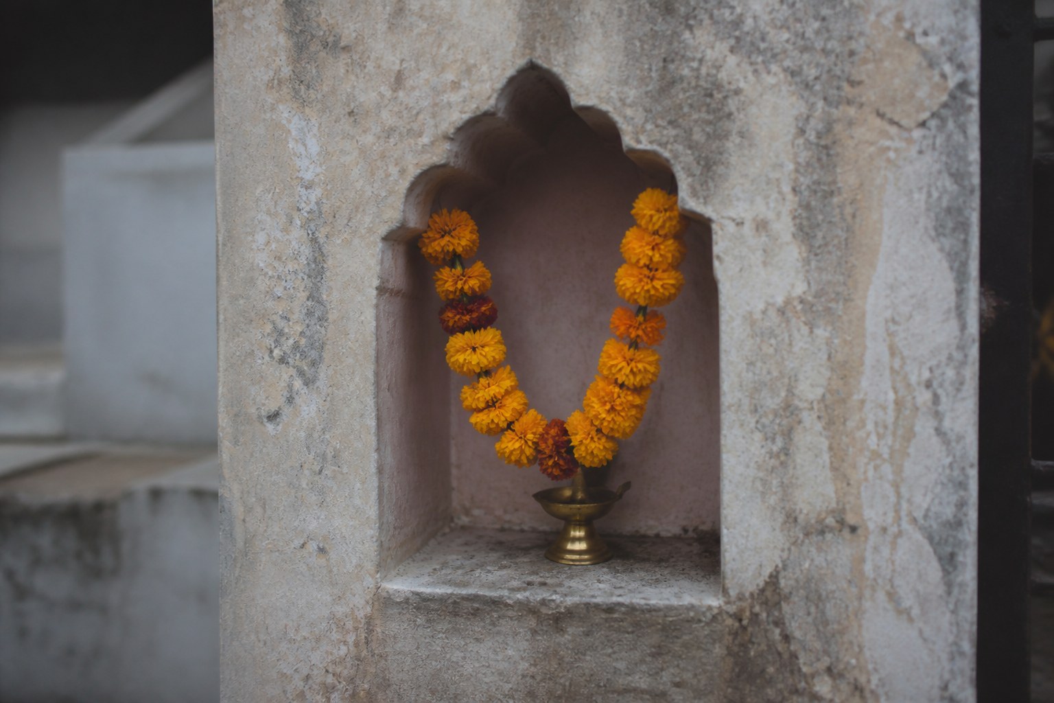 A stone wall niche holding a small brass oil lamp and a marigold garland