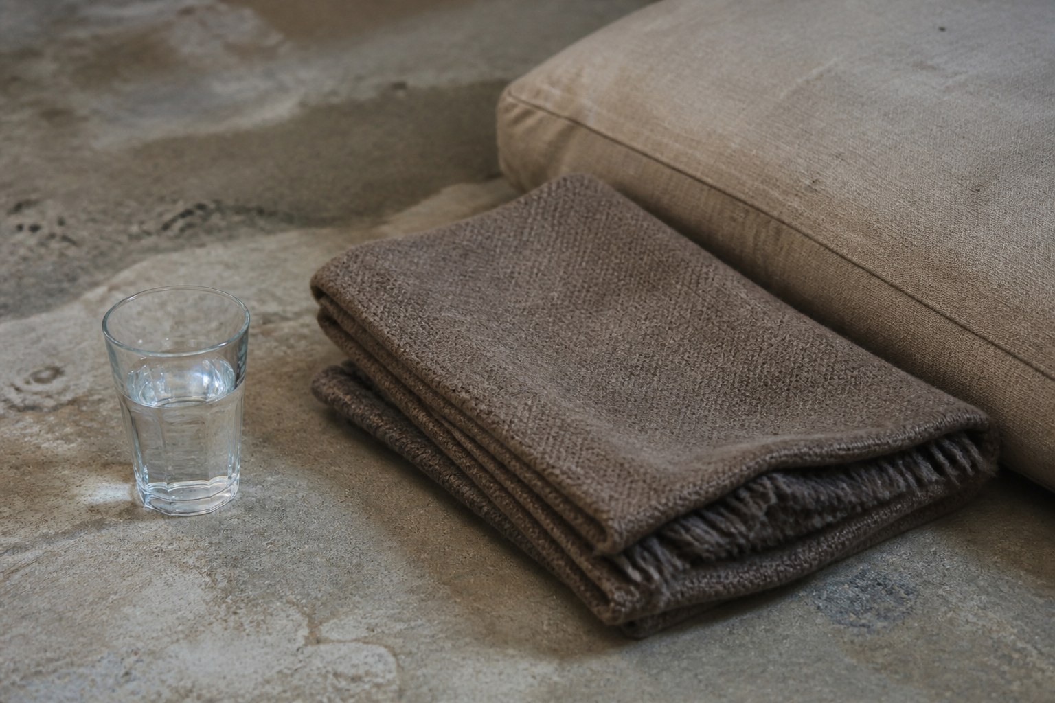 A glass of water and a folded blanket on the floor beside the edge of a cushion