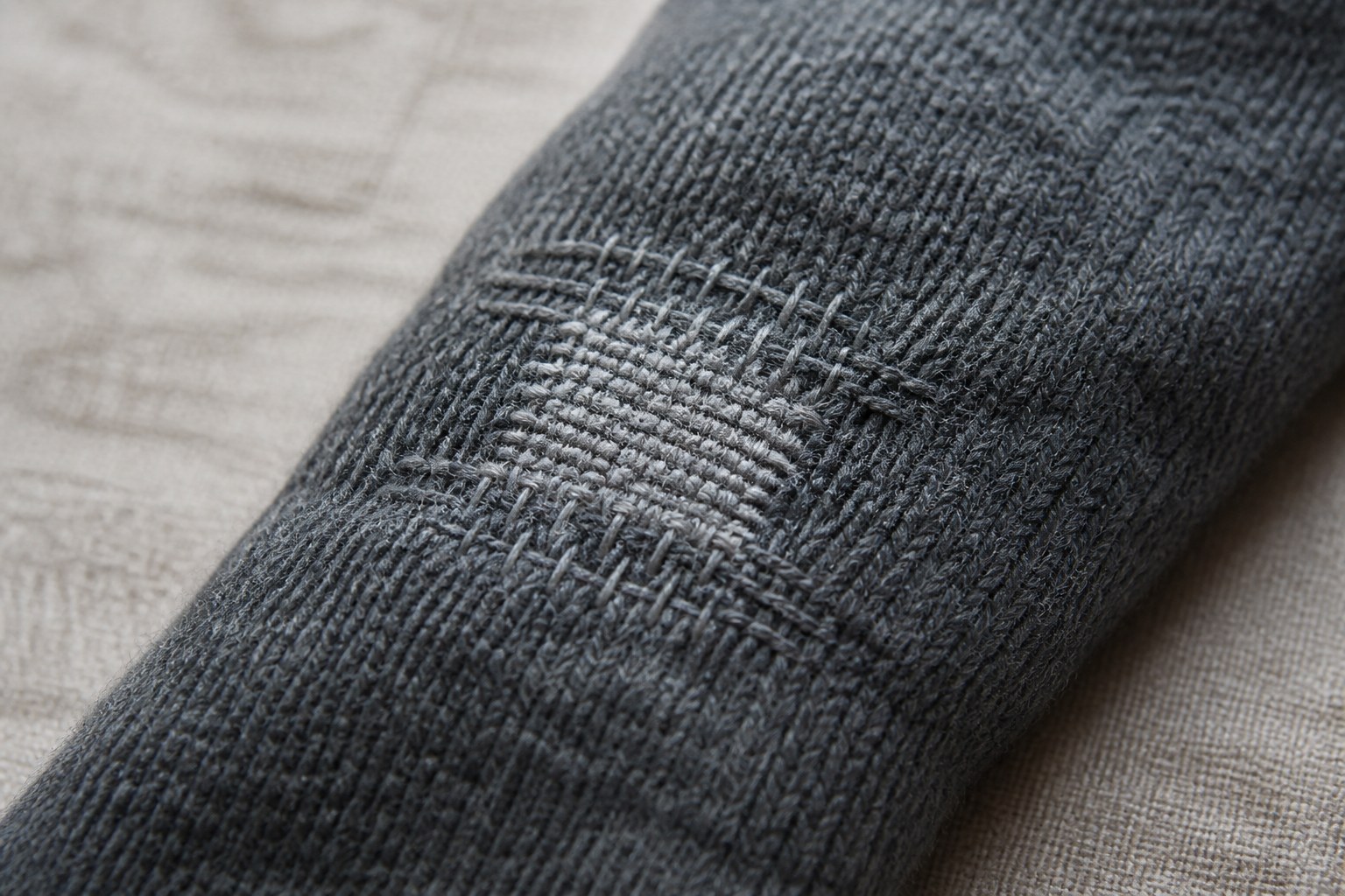 A visible darn repairing a hole across a knitted sleeve