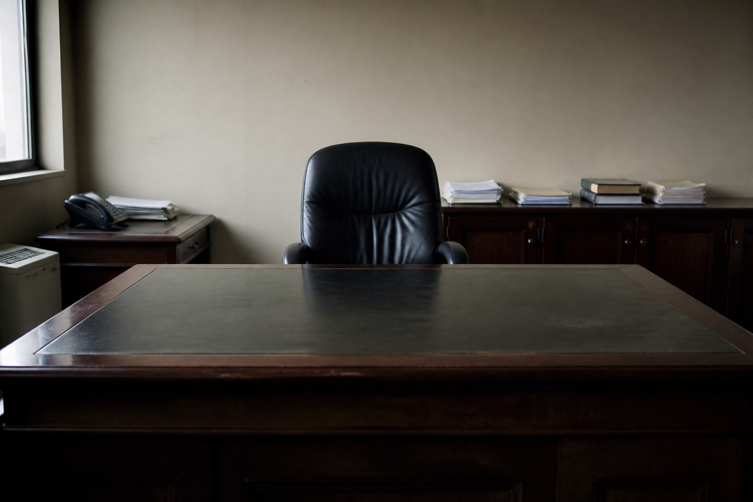 A large empty desk with a single leather chair behind it in a bare office
