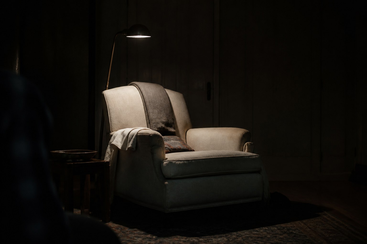 A reading lamp lit over a single armchair in an otherwise dark room
