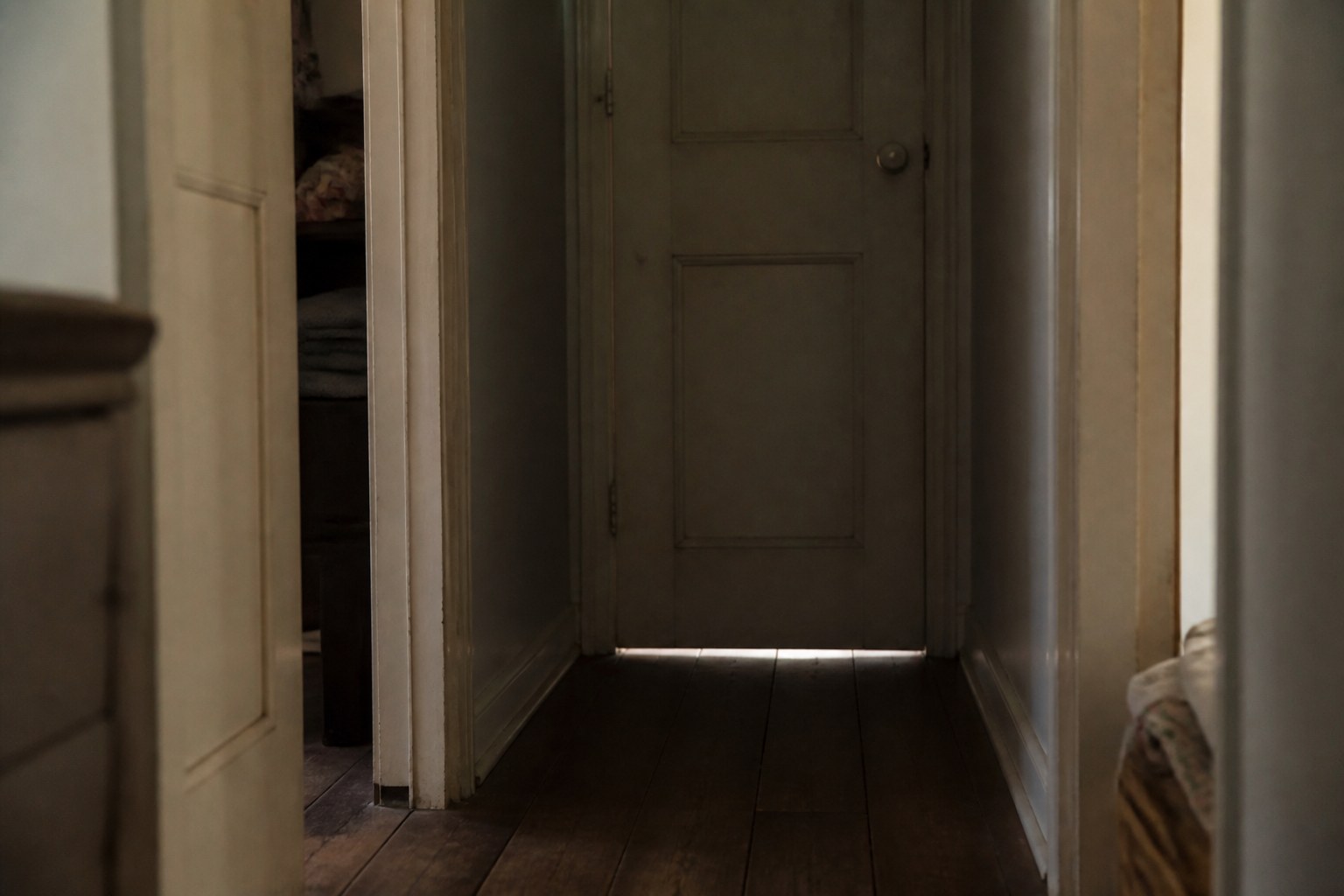 A closed internal door in a dim hallway with light showing underneath