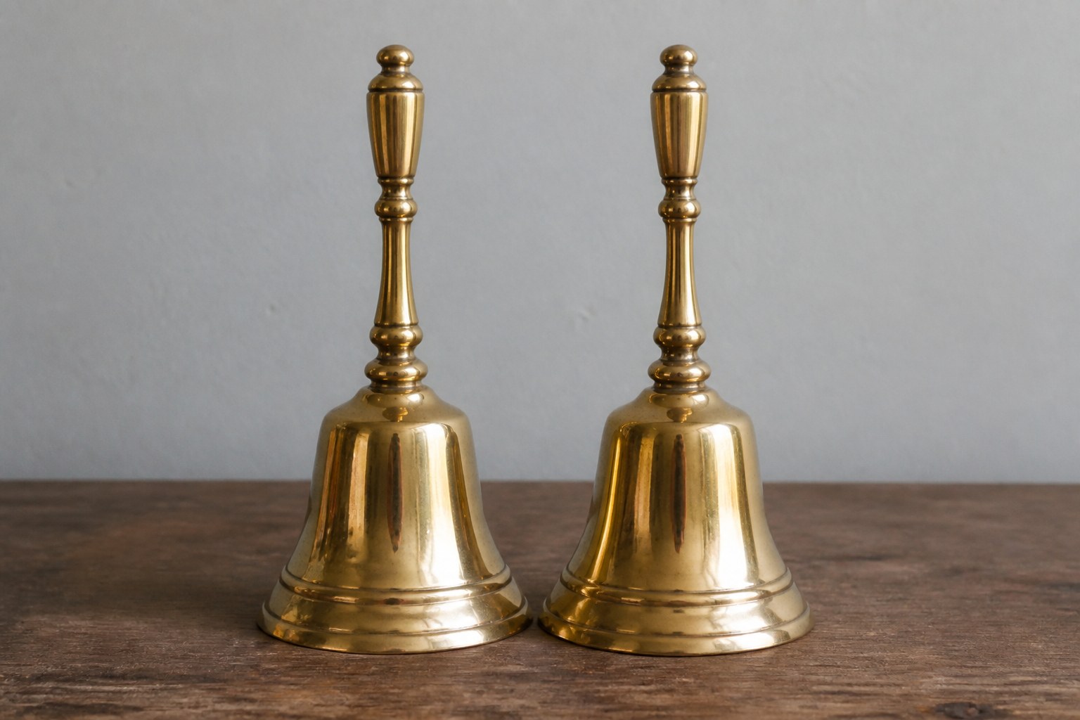 Two identical brass handbells standing side by side on a plain desk