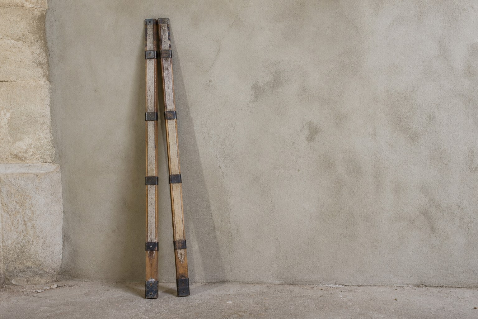 Two matched wooden surveyor's levelling staffs leaning together against a rendered wall