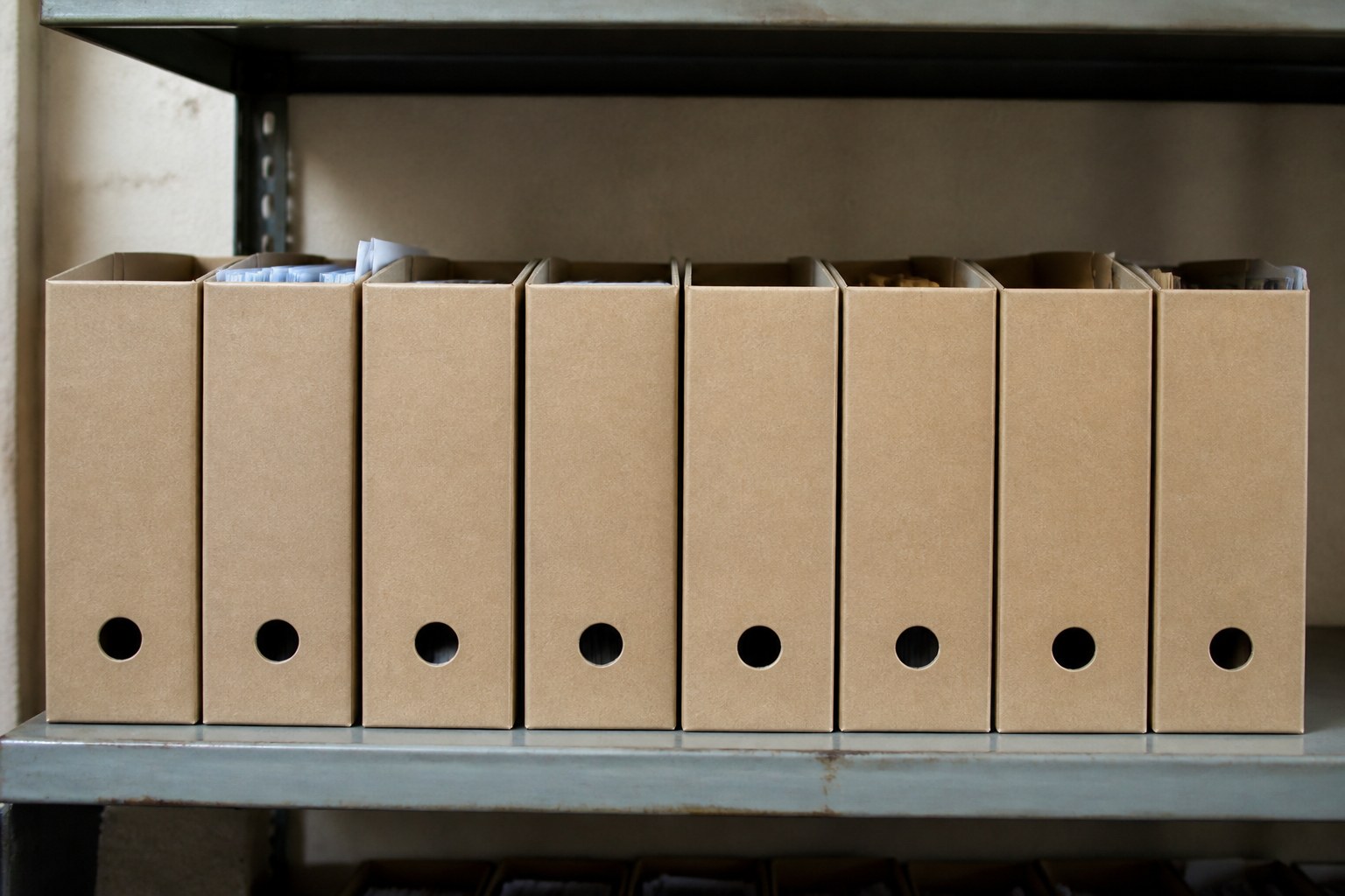 A row of identical archive boxes with blank spines on a shelf