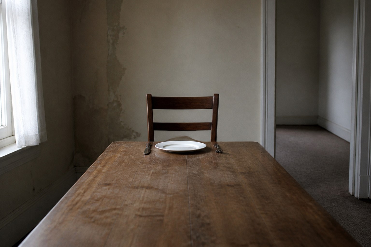 A single chair at a long table laid for one place in an empty room