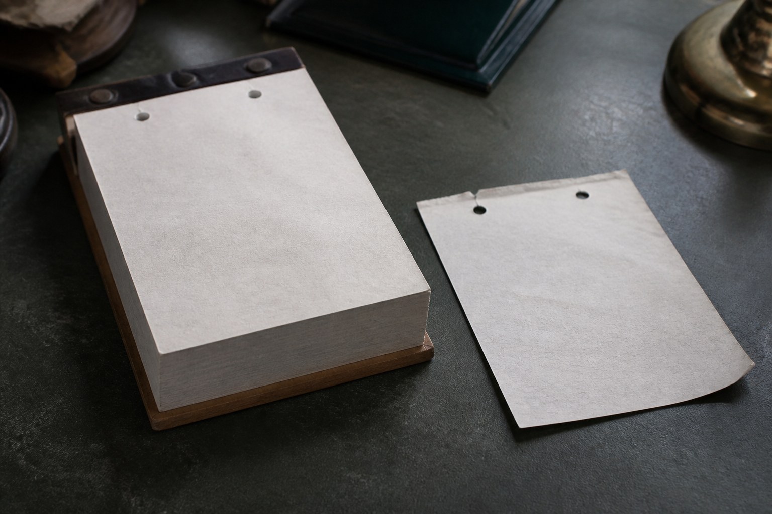 A single blank leaf torn from a tear off desk calendar block, lying beside the block itself