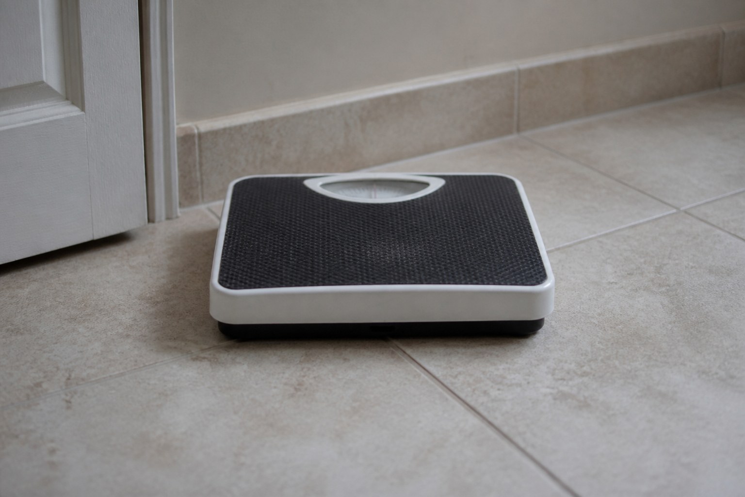 A plain bathroom scale standing empty on a tiled floor