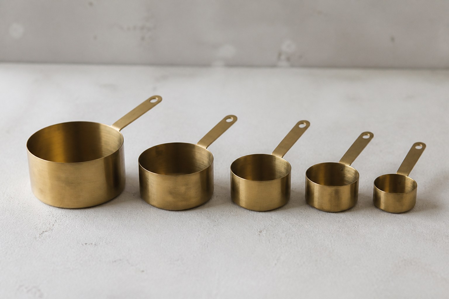 A set of nesting brass measuring cups taken apart and arranged in order from largest to smallest