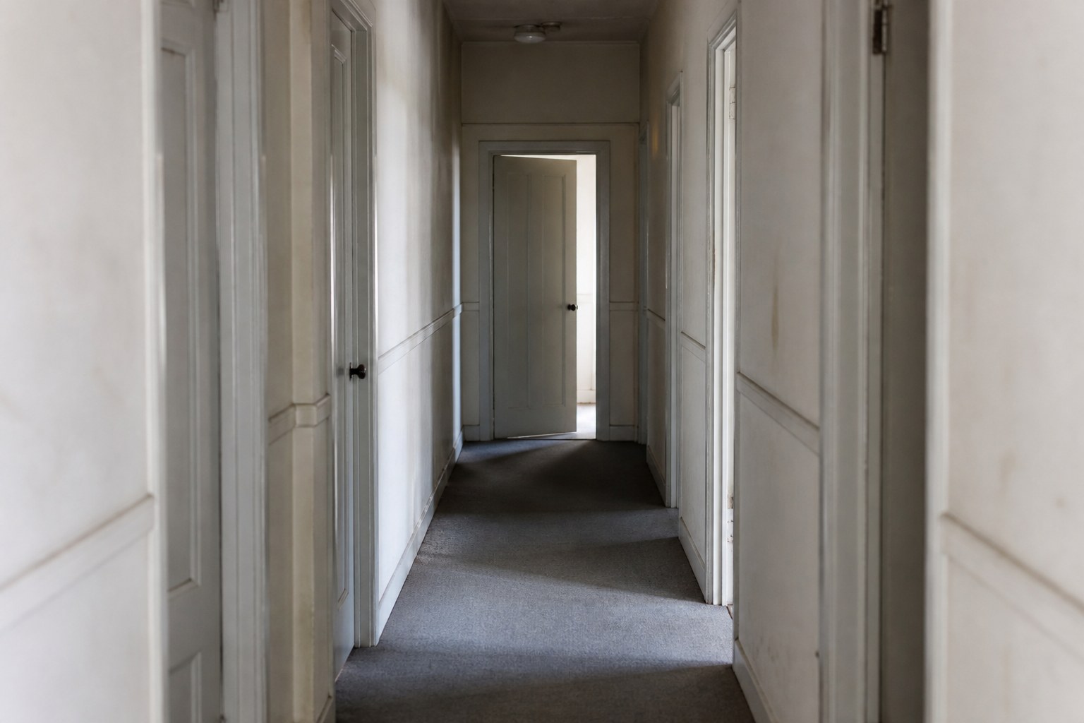 A corridor of closed doors with one standing slightly ajar at the far end