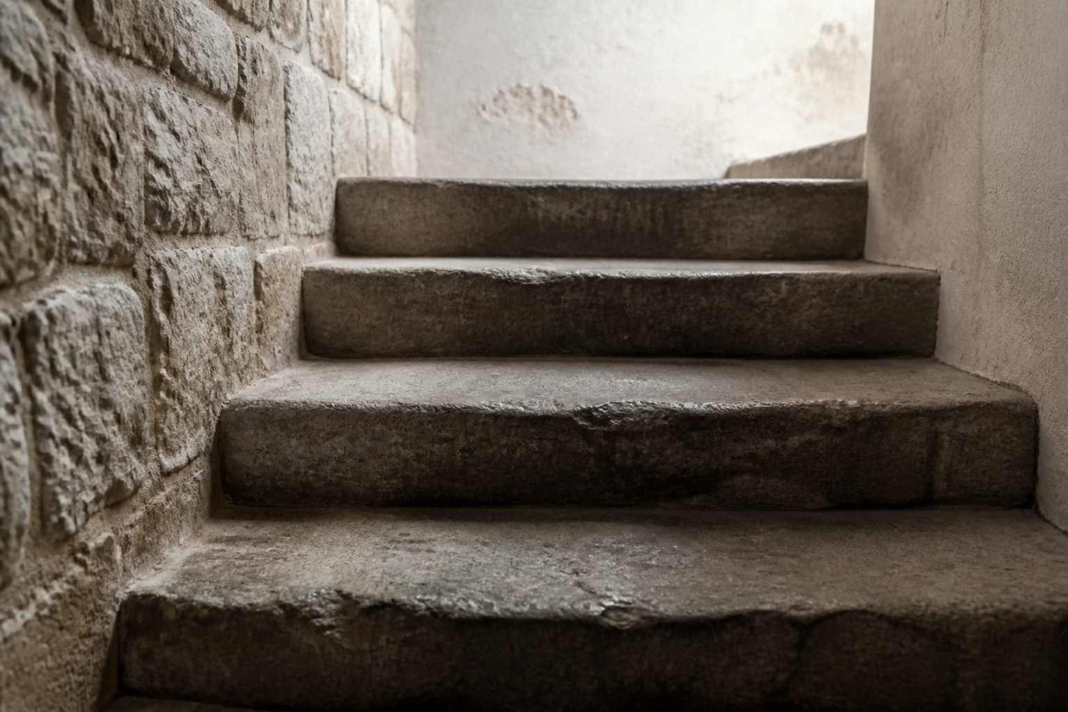 Four broad worn stone steps rising in a narrow stairwell in side light