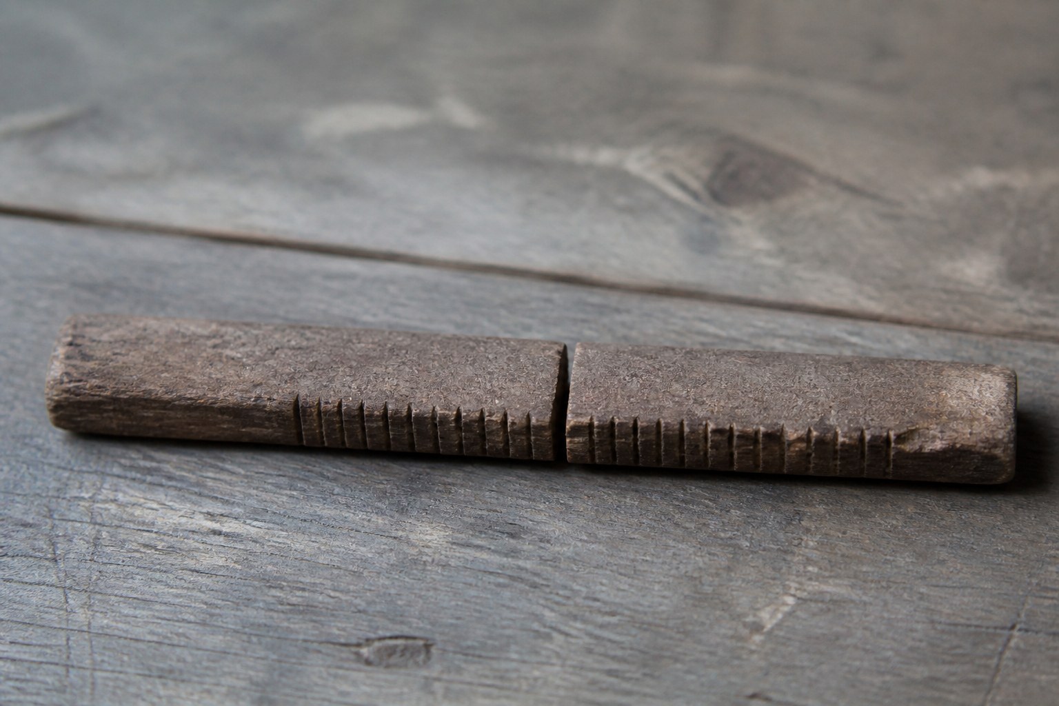 Two matching halves of a split wooden tally stick lying together so their notches line up