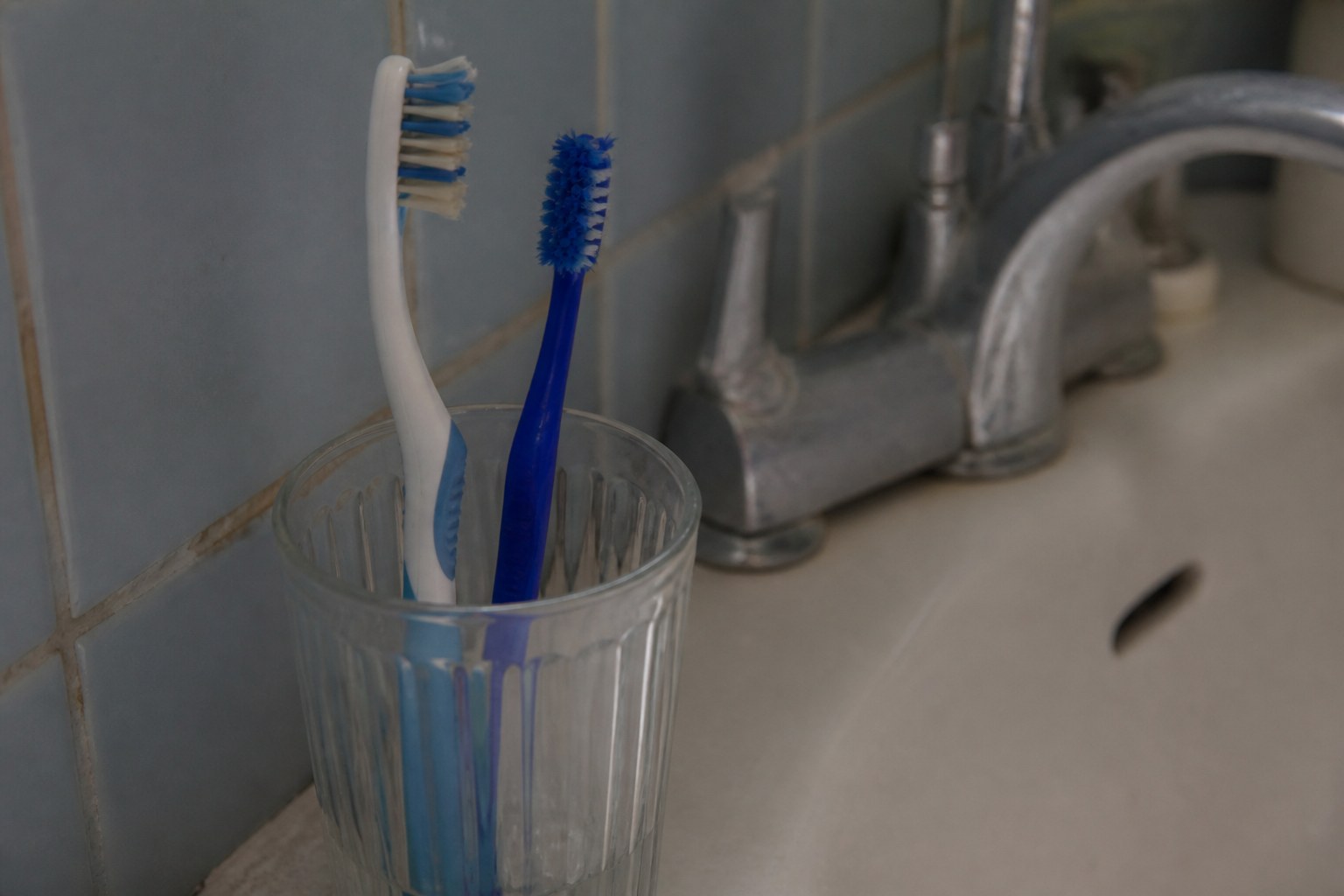 Two toothbrushes standing in one glass beside a bathroom sink